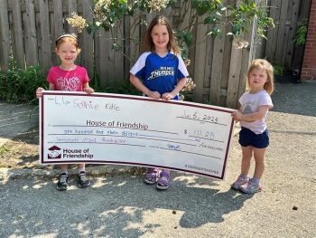 Lila, Sophie, and Edie are standing outside holding a large HOF check.
